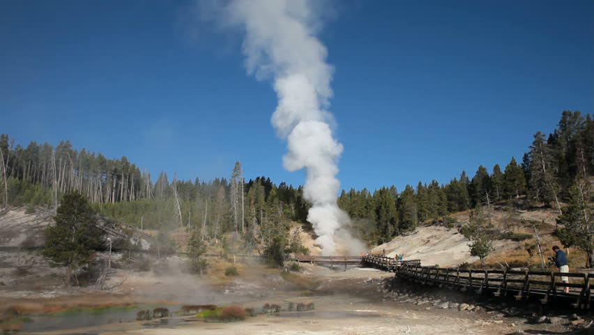 Spectators visit eruption of Dragon Mouth Geyser in Yellowstone National park, Wyoming. Steam and water blowing from ground. Hot steam geothermal feature.