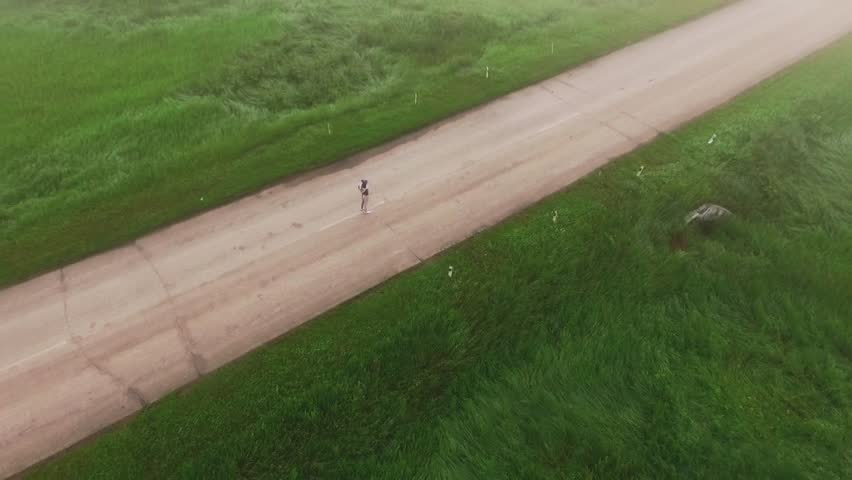 Drone rotating above girl stretching and running in countryside
