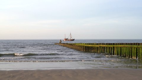 Waves and Groyne with a fishing Cutter  in the Background at Wangerooge Island North sea Germany