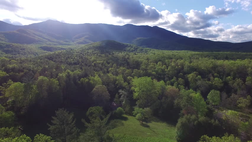 Aerial push of the Blue Ridge Mountains, sky, and surrounding forest in North Carolina. A cabin is seen in the lower half of the frame. 