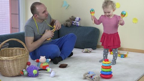 Father play toy guitar and baby daughter shake rattle. Family have fun at home. Static shot.