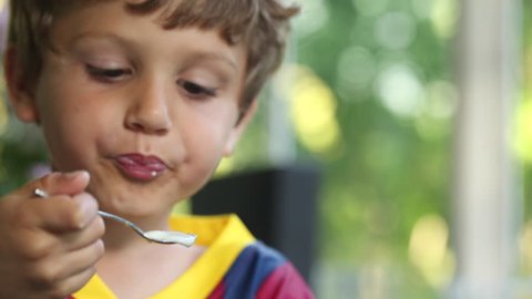 Young boy eating yogurt with spoon. 6 year old kid eating supper dessert