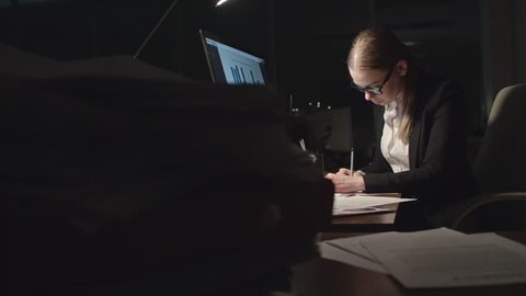 Tired young businesswoman analyzing financial statistics in dark office at night, taking off her glasses and trying to concentrate, shot on Sony NEX700 + Odyssey 7Q