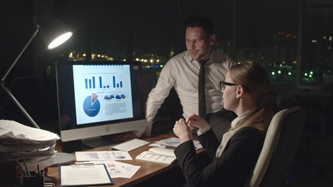Medium shot of business man and woman analyzing financial statistical data on computer screen in dark office at night, medium shot on Sony NEX700 + Odyssey 7Q