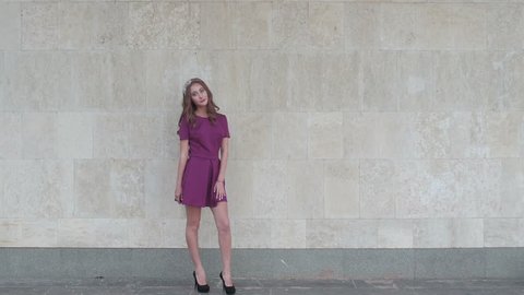 Young attractive woman posing near wall for fashion photographer