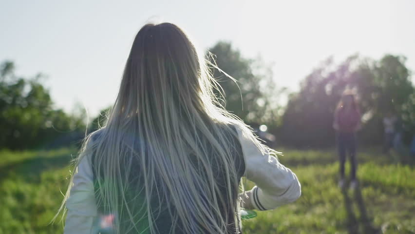 Young woman in blue jeans and white sneakers Throwing A disc at summer day on meadow in high hill towards the sun, slow motion