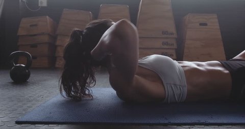 Sportswoman on exercise mat doing situps in gym. Muscular female athlete doing abs workout.
