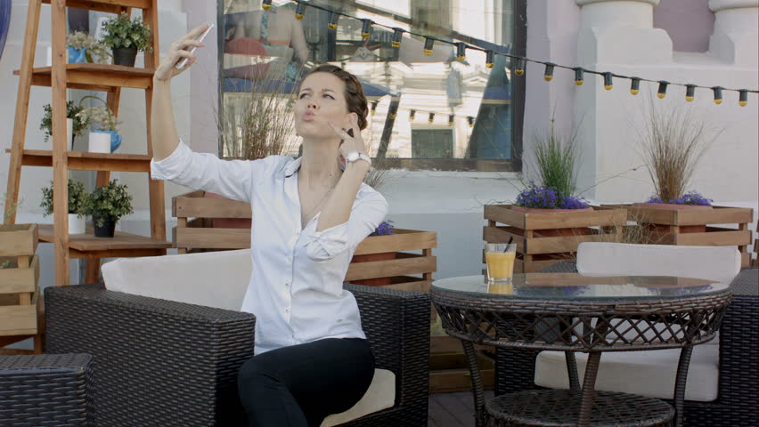 Young woman making self portrait using smartphone. girl making selfie. woman in cafe. woman alone. self portrait in cafe outdoors. smile. smilimg. gadget. self portrait. coffe break. coffee time