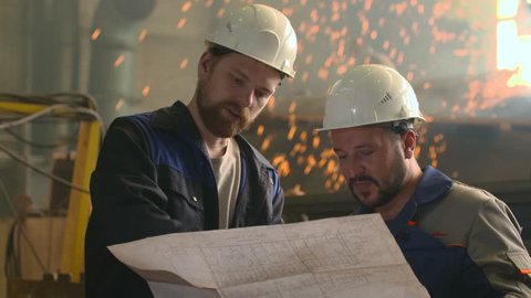 portrait of two engineers explore and discuss project in heavy industry factory. welding background