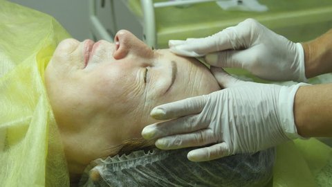 Hands of beautician are preparing the skin for the procedure or cleaning after the procedure. Old woman lies and getting eyelash makeup at beauty salon. Applying Permanent Make up on eyelash. 