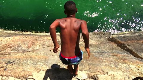Young Brazilian man dives from a rock at the Leme end of Copacabana Beach into deep green waves Rio de Janeiro, Brazil