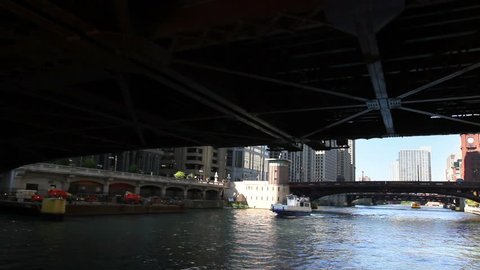 View from a boat as it passes underneath a bridge and passes another boat on the Chicago River in the middle of downtown Chicago.