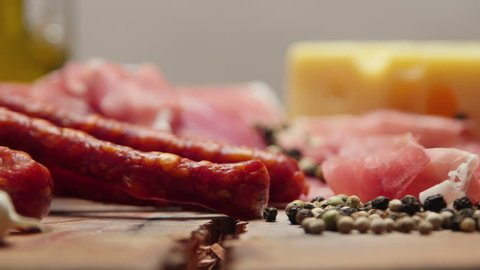 Close up of thin slices of prosciutto with dry raw sausages and swiss cheese on wooden cutting board