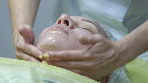 Beautician applying facial mask on a beautiful girl face at beauty salon. Woman having a facial care. Use of face masks in cosmetology. Close-up of a young woman with silicone mask on her face