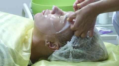 Beautician applying facial mask on a beautiful girl face at beauty salon. Woman having a facial care. Use of face masks in cosmetology. Close-up of a young woman with silicone mask on her face