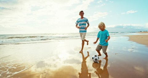 Father and son having fun on the beach at sunset, kicking soccer ball in slow motion Video Stok