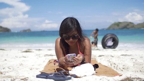 Asian woman sunbathing on beach and using smart phone