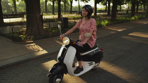Young beautiful girl riding around city on scooter at sunrise. Slow motion. స్టాక్ వీడియో