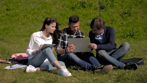 College Students Using Laptop And Tablet On Campus Lawn, Outdoor Study Concept