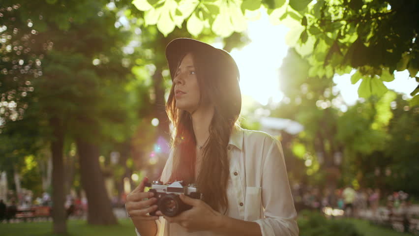 Young beautiful girl in hat photographing in city park. Slow motion.
