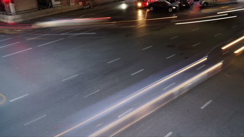 Time lapse of traffic long exposure light trails across road junction during rush hour, from evening to dusk, unrecognizable faces, logos, and license plates