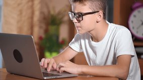 Teen boy with glasses working on laptop computer in living room. Young programmer surfing internet - watching video and game.