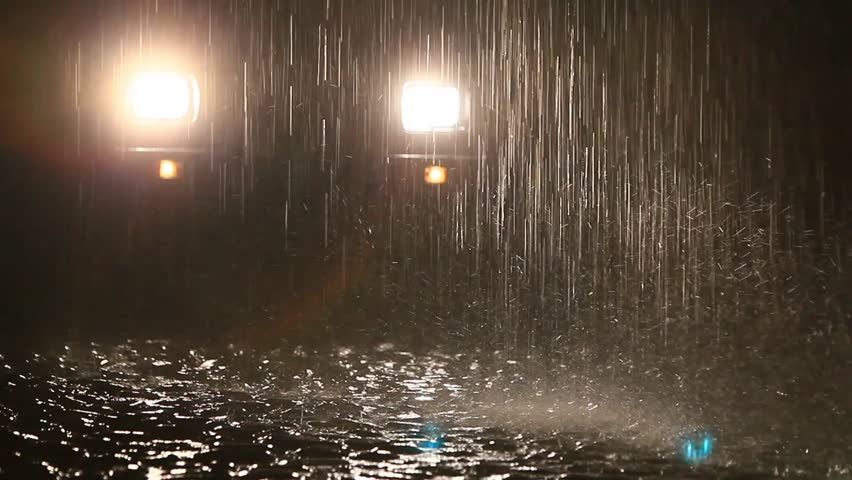 Heavy rain in Ecuadorian tropical forest by night, shot against car headlights