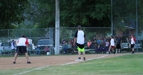 FOUNTAIN GREEN, UTAH - JUL 2016: Softball game third base run to home. Rural community. Team spirit and teamwork with youth, teenagers and parents. Sports, recreation and healthy exercise.