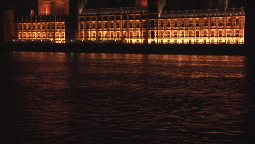 Tilt up from the River Thames to Big Ben with the House of Parliament illuminated with golden lights at night London UK