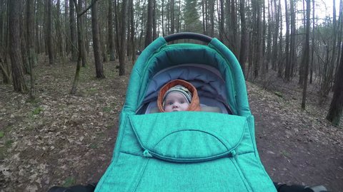cute little baby girl look around in the wood driving in buggy. Camera hang on handle.
