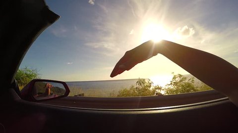 SLOW MOTION CLOSE UP: Driving in red convertible, arm outside of car playing with wind against the sunset sky. Unrecognizable female waving with her hand in wind on summer vacation in Hawaii island