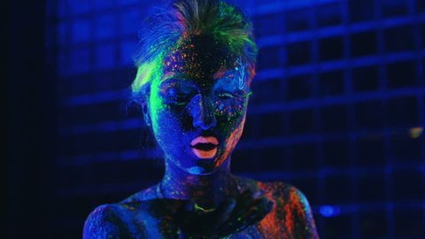 girl in ultraviolet light blows pink fluorescent powder with palm