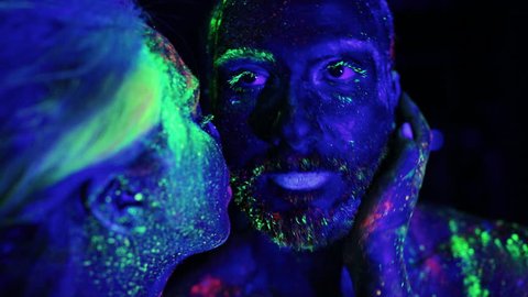 Couple in love painted fluorescent powder kiss under ultraviolet light.