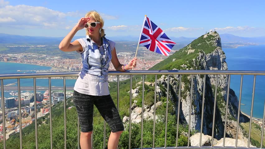 Tourist woman holding an English flag observes one of the famous monkey of Gibraltar from the top of Gibraltar Rock, in the Upper Rock Natural Reserve.