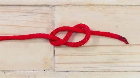 4K stop motion figure eight knot made from red synthetic rope, tightening on wooden background