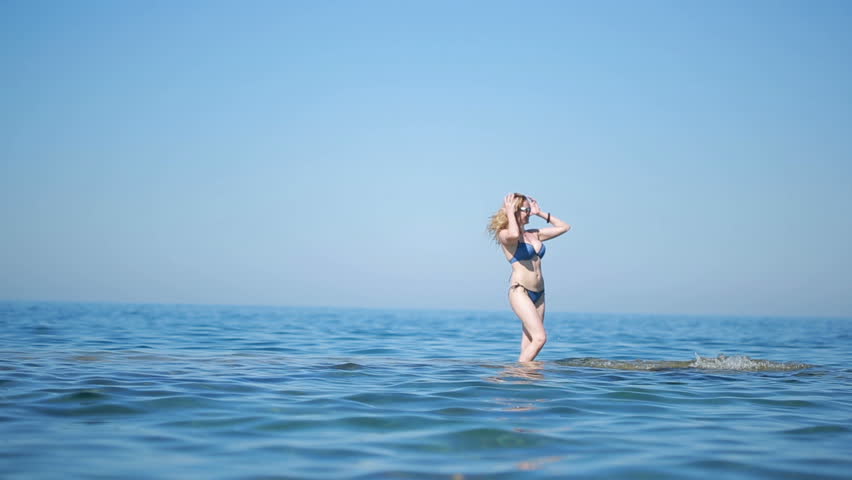 Sexy girl in blue bikini having fun standing in water. on the beach in the waves