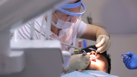 Dentist at work in dental unit with a nurse and a man lying patient.