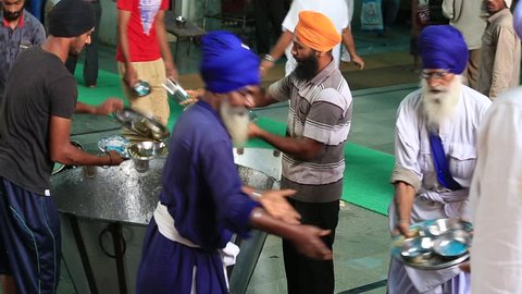 AMRITSAR, INDIA - SEPTEMBER 27, 2014: Unidentified poor indian people clean dishes at a soup kitchen in the Sikh Golden Temple