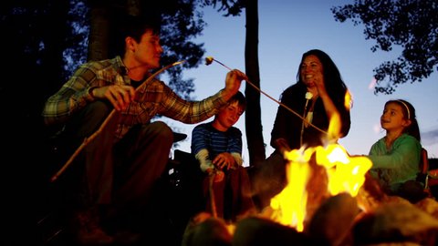 American Caucasian family toasting and eating marshmallows on holiday outdoors