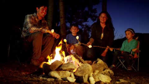 Portrait of happy American family toasting smores in woodland on vacation