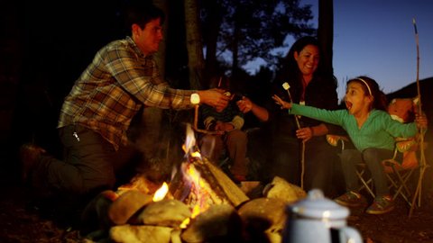 Happy American Caucasian parent and children enjoying toasting smores outdoors
