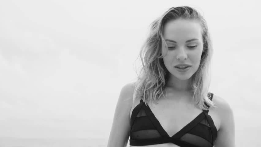 Beautiful glamour woman wearing black swimwear smiling and posing on a beach in a sunny summer day with folding hand fan over sea and sky background - black and white video in slow motion