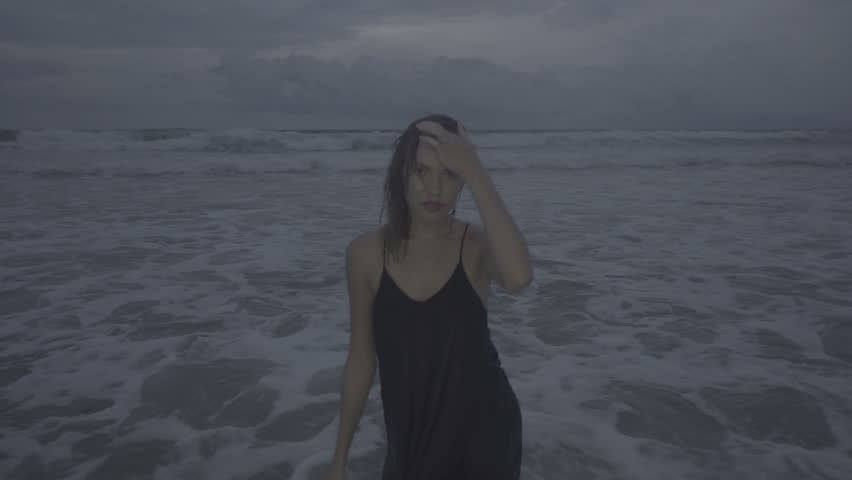 Beautiful blonde glamour woman wearing black dress posing on a beach in a late summer afternoon with wet hair over sea and sky background