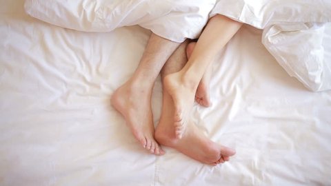 a man and a woman in bed. male and female legs top view, white linens