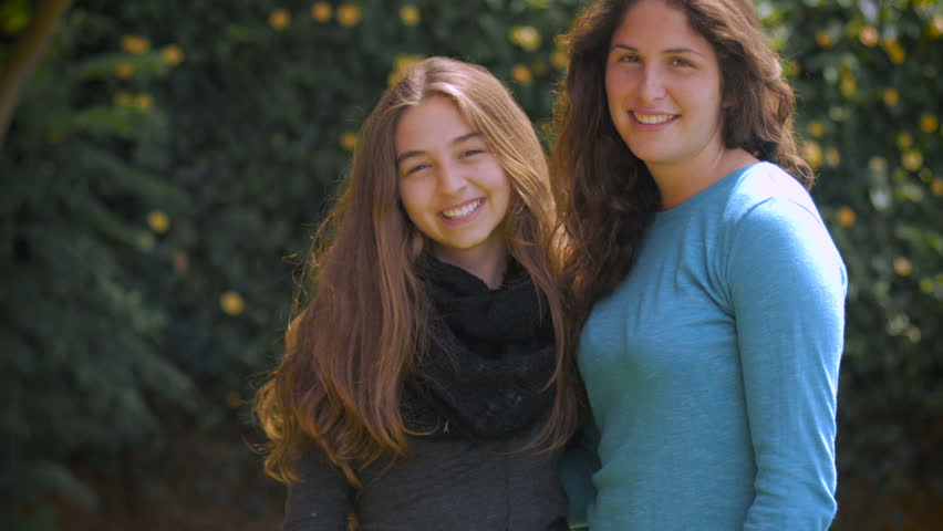 Two attractive teenage sisters hug, smile, and laugh for the camera in slow mo
