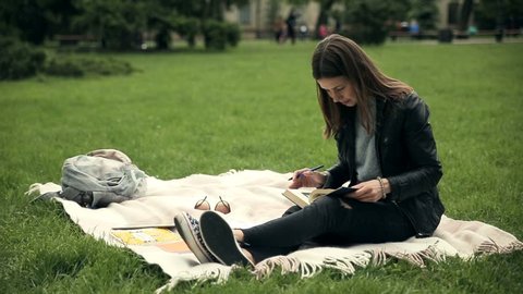 Adorable female student reading tutorial outdoors.