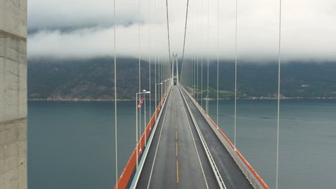 Aerial Shot Car Crossing Suspension Bridge across River in Norway. Weather is Foggy and Cloudy. 