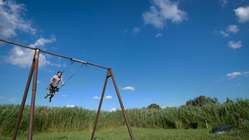 A young woman is swinging on a swing at a green field.