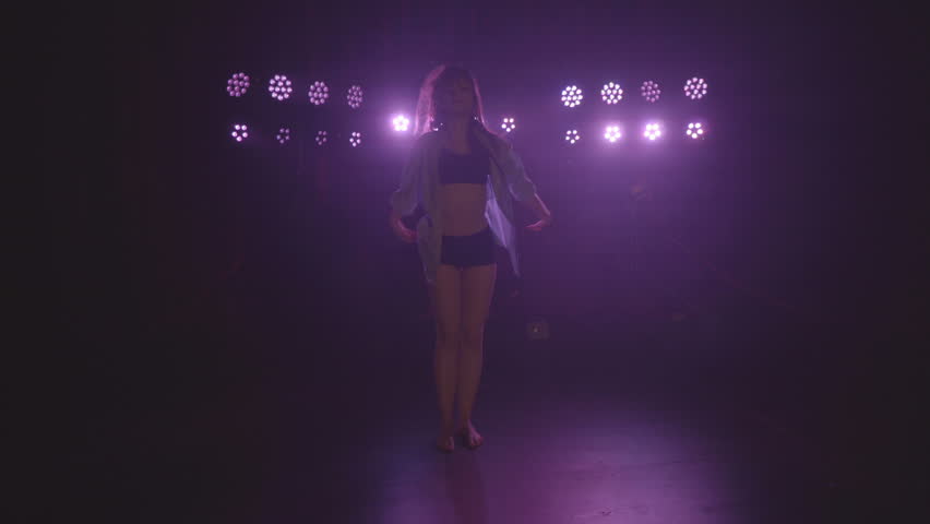 Silhouette of woman solo freestyle performance dancing barefoot on a dark stage with lights changing colours and smoke