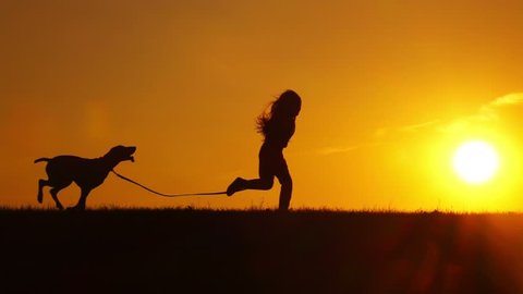 Pretty young girl running with her dog outdoors on sunset backlit by sun, slow motion.
